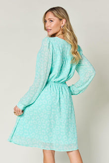Woman wearing a mint green ruched long sleeve dress with a leopard print design, showcasing the back view.