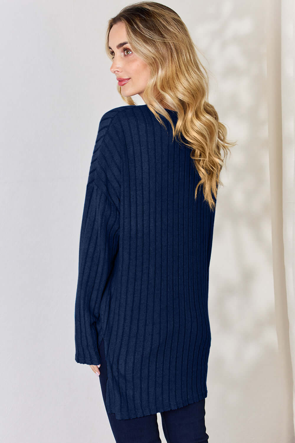 Model wearing a navy ribbed long sleeve high-low T-shirt from the back, showcasing its buttoned design and relaxed fit.