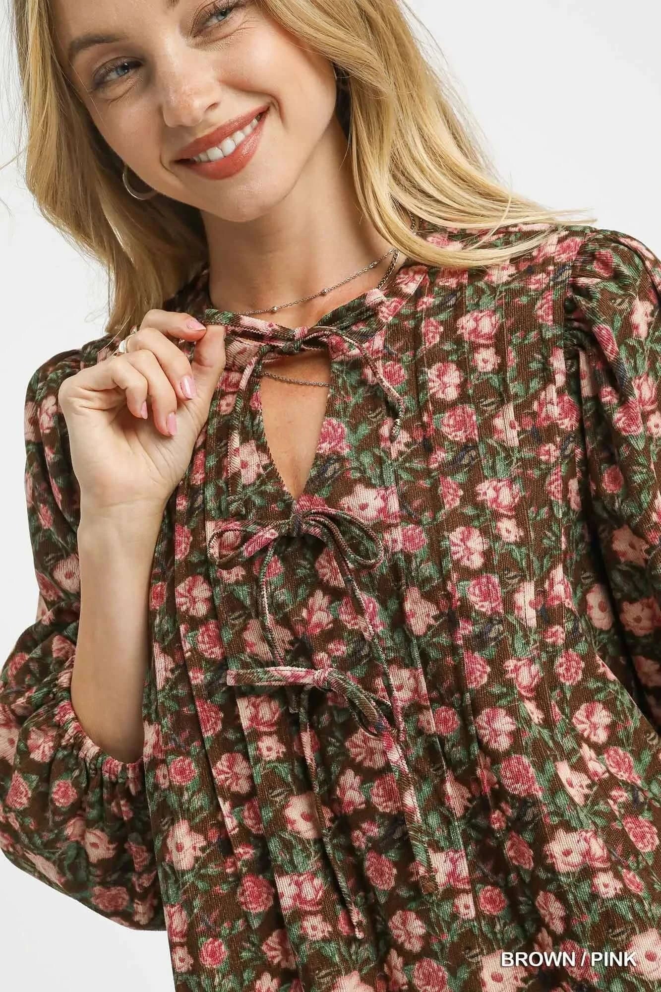 Close-up of a woman smiling in a floral tie-neck babydoll dress featuring a brown and pink pattern.