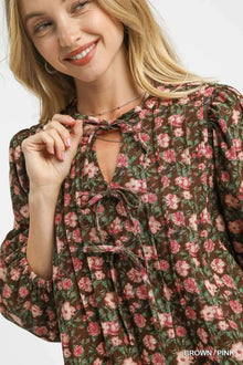 Close-up of a woman smiling in a floral tie-neck babydoll dress featuring a brown and pink pattern.