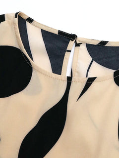 Close-up of the neckline and fabric design of a Tied Pleated Printed Cap Sleeve Dress featuring black and beige patterns.