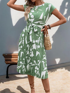Tied pleated printed cap sleeve dress in green with abstract patterns, paired with a woven bag, perfect for summer outings.