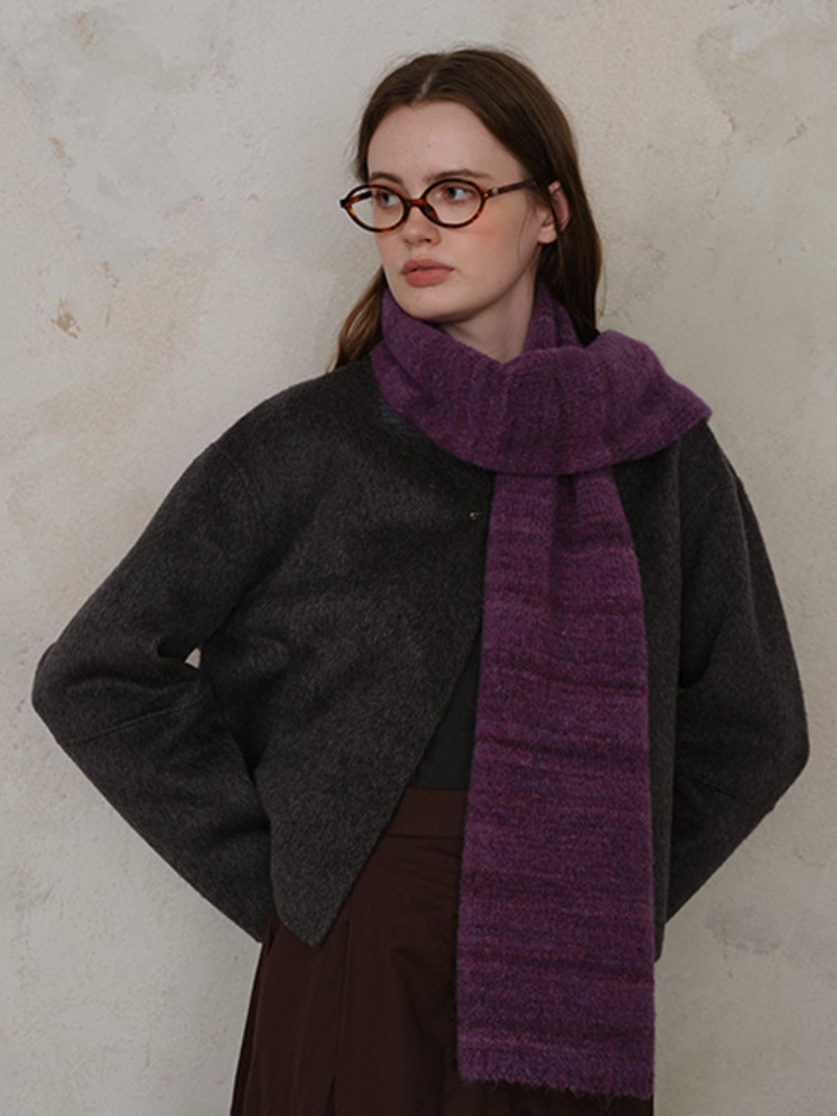 Woman wearing a purple striped detail knit scarf, paired with a dark jacket and stylish glasses, showcasing elegance.