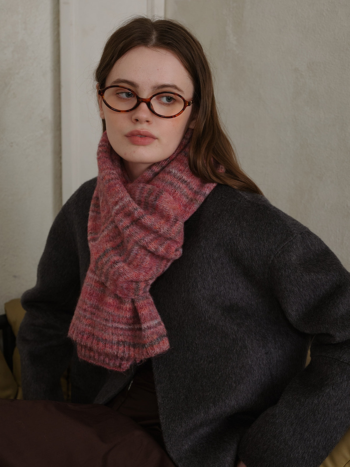 Woman wearing a pink striped detail knit scarf, paired with a dark sweater, showcasing cozy winter fashion.