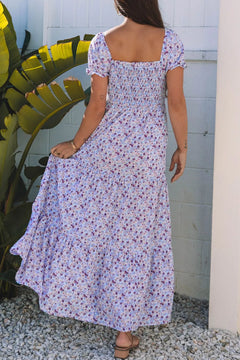 Model in a tiered floral shirred high waist maxi dress, showcasing the back design amid tropical plants.