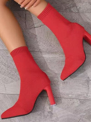 Red point toe block heel boots with sock-style design on wooden floor.