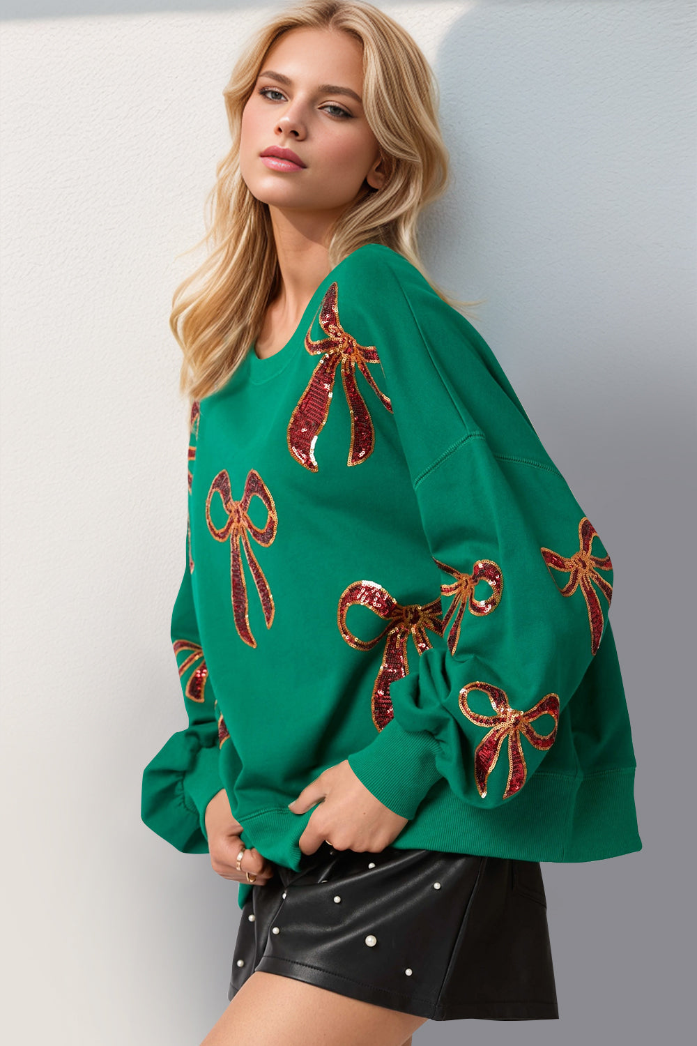 Stylish model wearing a green Double Take Sequin Bow Sweatshirt with festive sequin bow accents.