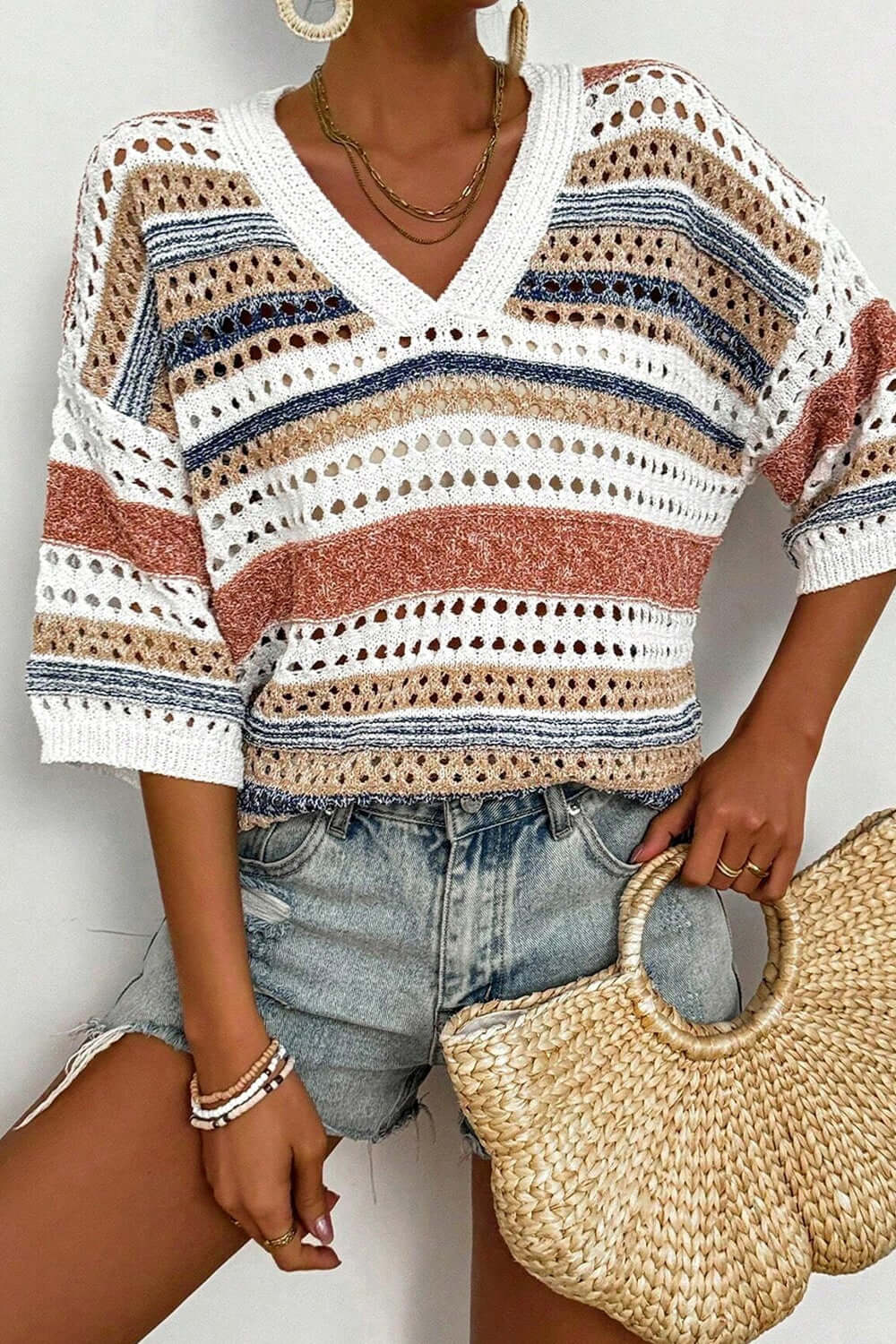 Striped hollow out half sleeve knit top in openwork design, paired with denim shorts and a straw bag.