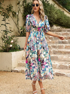Model wearing a colorful printed puff sleeve midi dress with floral pattern, styled with sunglasses and heels.