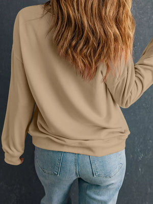 Back view of a woman in a beige drop shoulder sweatshirt, paired with blue jeans, highlighting a casual style.