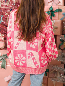 Woman wearing a pink Candy Cane Round Neck Long Sleeve Sweater against a festive backdrop of gifts.