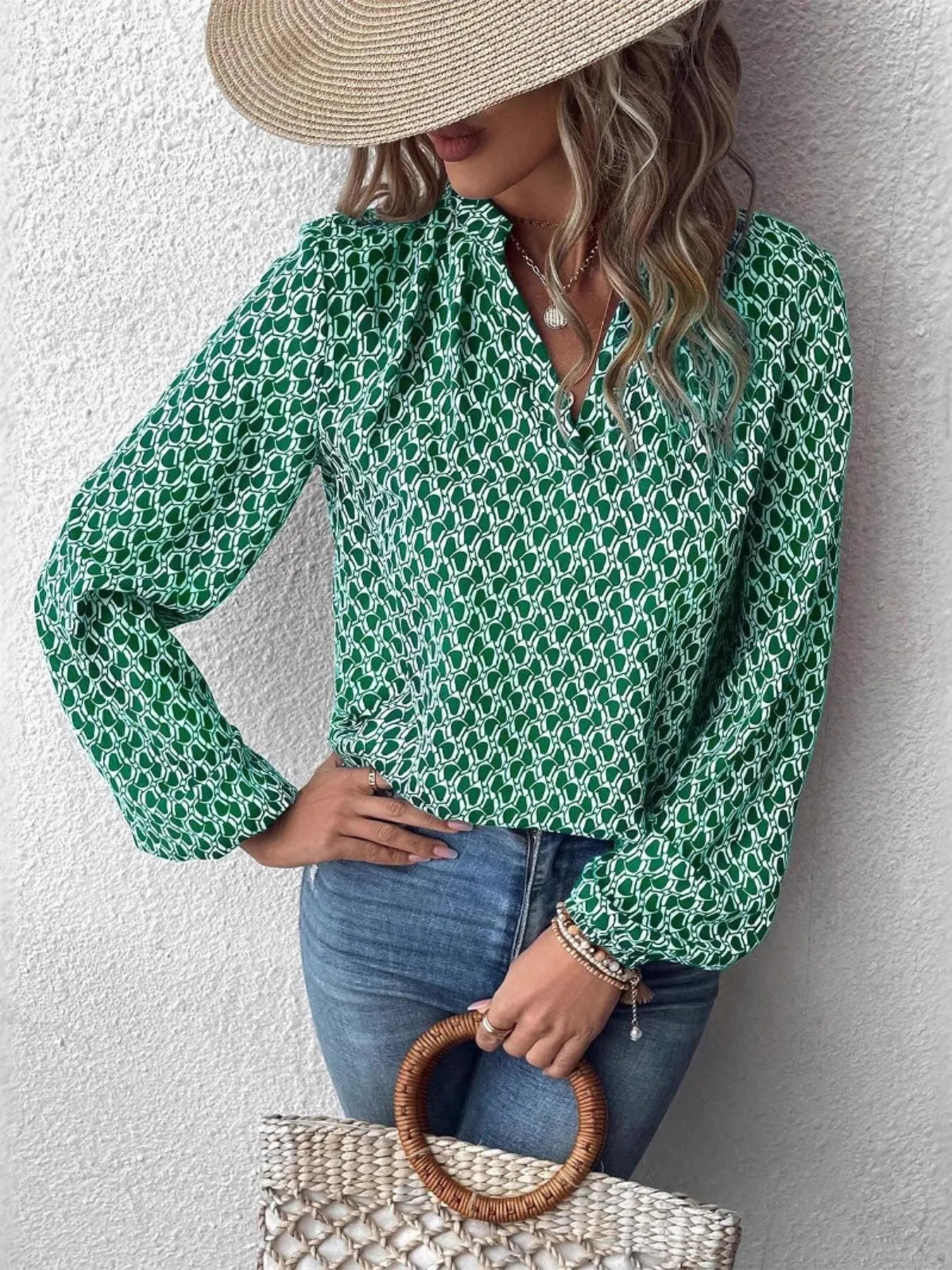 Model wearing a green printed notched long sleeve blouse with a straw hat, holding a woven bag.