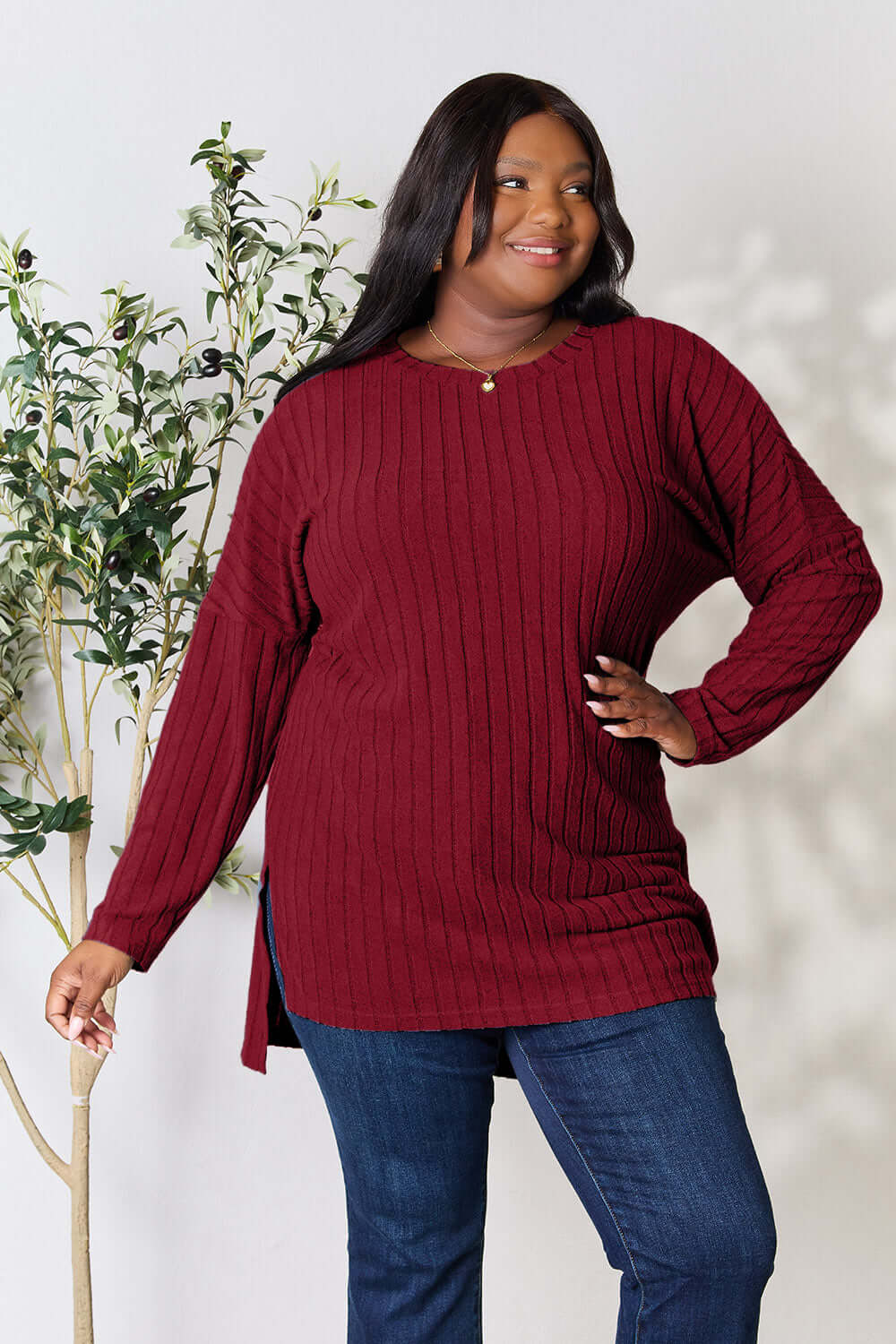 Model wearing a burgundy ribbed long sleeve slit top paired with jeans, showcasing a trendy high-low style.