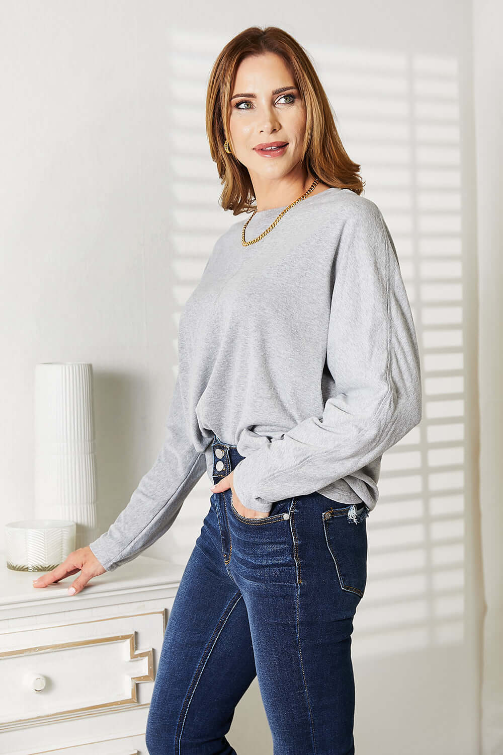 Double Take Seam Detail Round Neck Long Sleeve Top featuring a model in a light grey top and jeans.