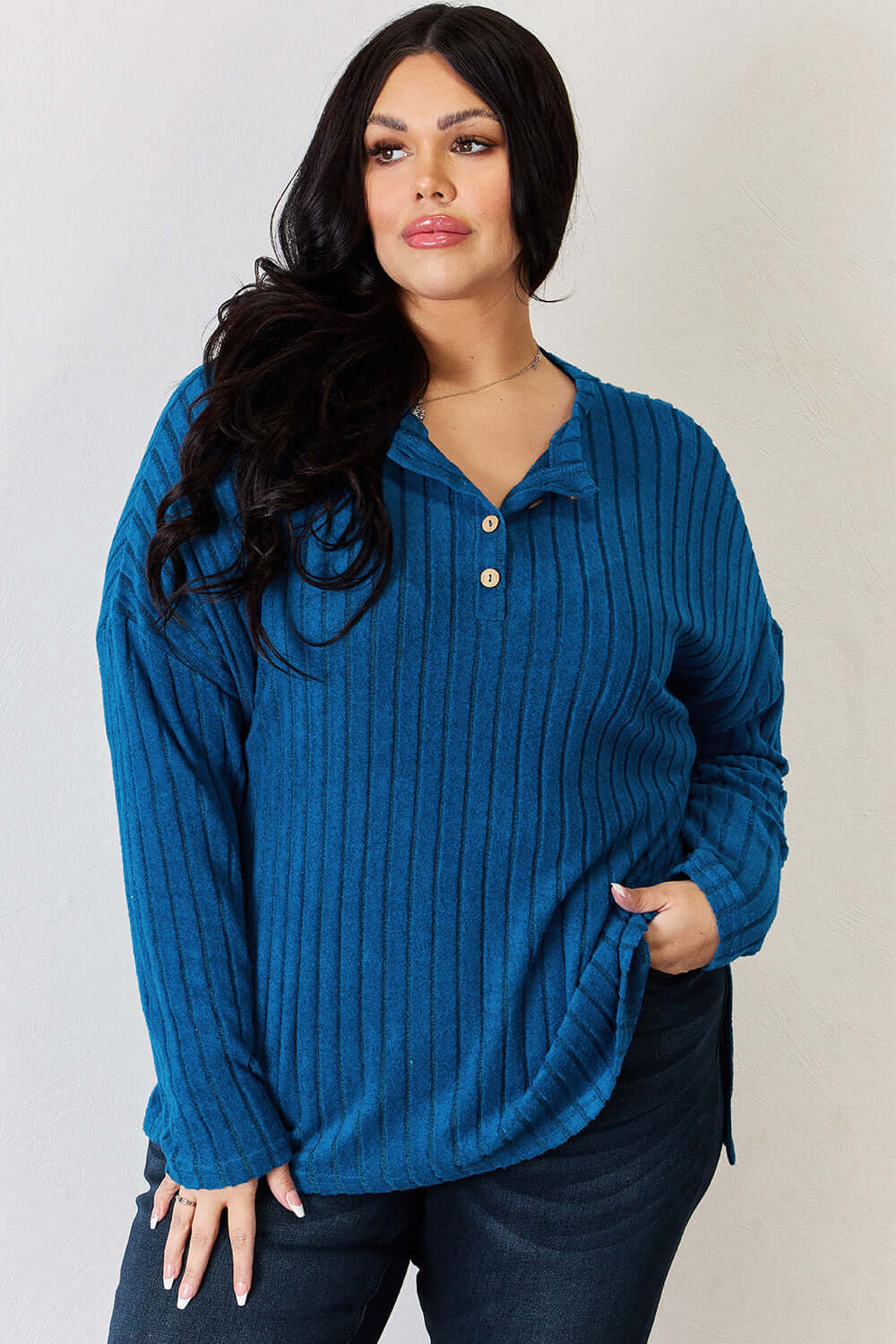 Curvy model wearing a blue ribbed long sleeve t-shirt with half buttons and high-low hem, styled with dark jeans.
