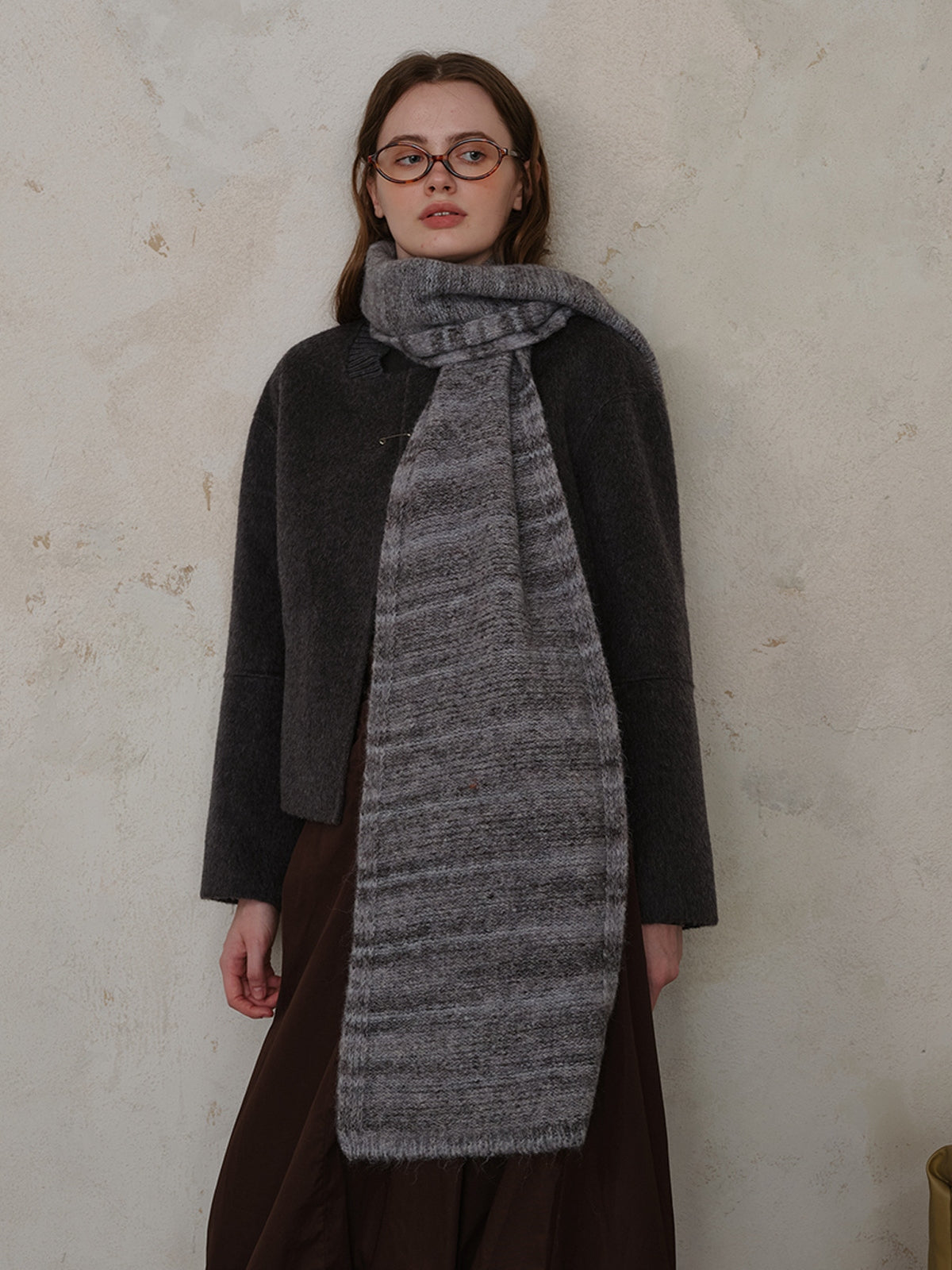 Woman wearing a striped detail knit scarf made of fur, styled with a chic outfit against a textured wall.