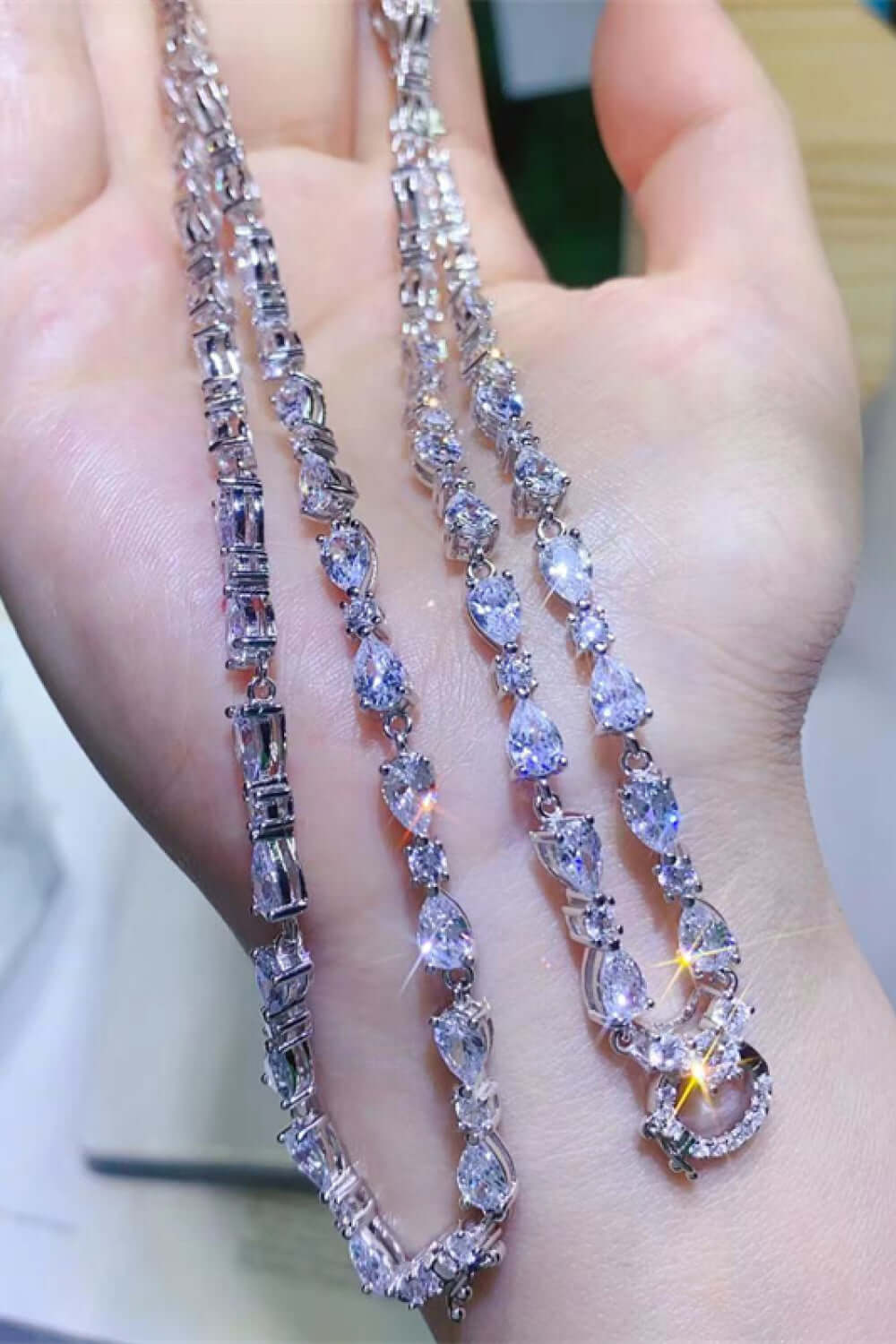 Elegant teardrop pendant necklace featuring sparkling moissanite stones on a hand, showcasing modern jewelry design.