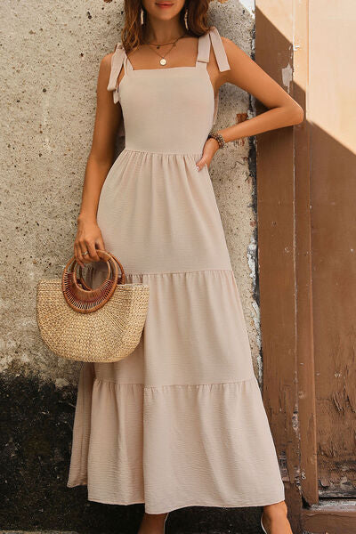 Woman wearing a tie shoulder smocked tiered dress, perfect for summer outings, paired with a stylish straw bag.