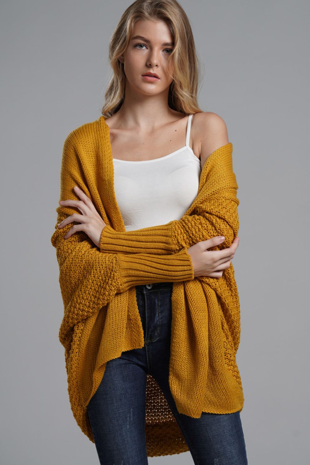 Model wearing a longline mustard cardigan with ribbed trim and open front, styled over a white tank top.
