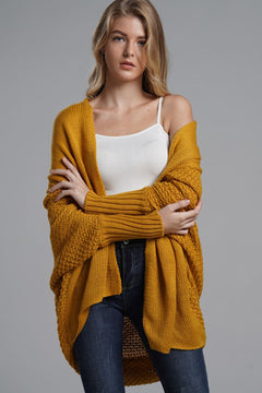 Model wearing a longline mustard cardigan with ribbed trim and open front, styled over a white tank top.