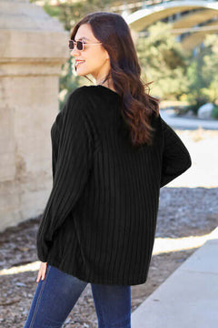 Woman in a black ribbed knit top with long sleeves, showcasing a casual style outdoors.