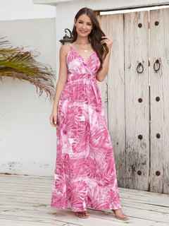 Model wearing a printed surplice spaghetti strap dress in pink tropical pattern, standing on a wooden deck.