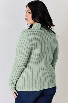 Back view of a plus-size woman wearing a ribbed mock neck long sleeve t-shirt in soft green.
