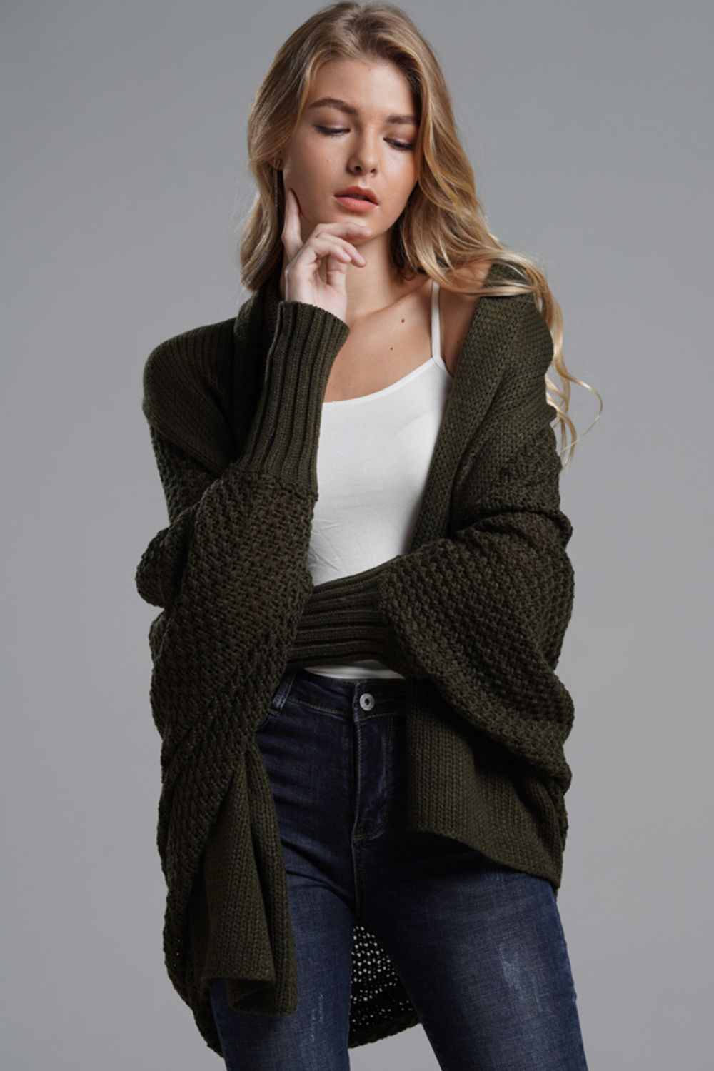 Model wearing a longline dolman sleeve cardigan in olive green, styled over a white top with dark jeans.