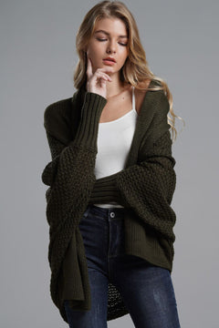 Model wearing a longline dolman sleeve cardigan in olive green, styled over a white top with dark jeans.