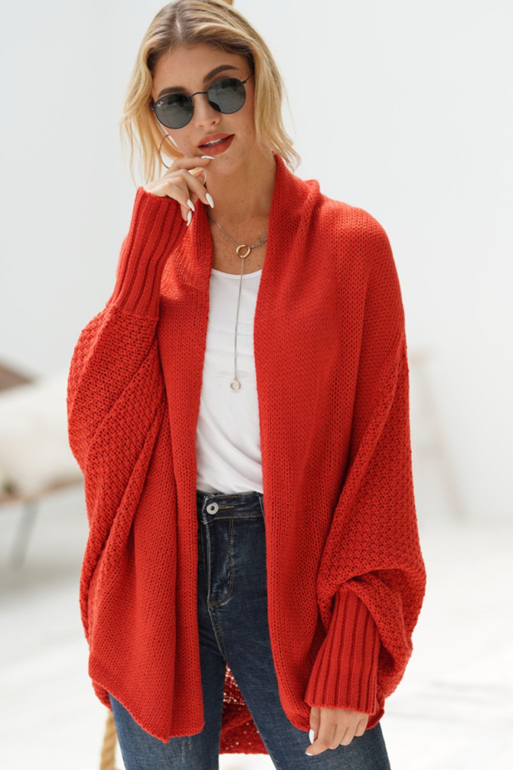 Woman wearing a longline open front ribbed cardigan in red paired with sunglasses and casual outfit.