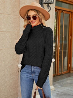 Stylish woman in a black cable-knit mock neck sweater, paired with jeans and a wide-brimmed hat, posing outdoors.