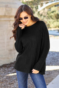 Model wearing a black ribbed long sleeve knit top, styled with sunglasses and blue jeans outdoors.
