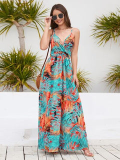 Woman modeling a colorful printed surplice spaghetti strap dress against a tropical background.