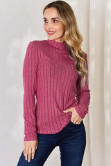 Model wearing a pink ribbed mock neck long sleeve t-shirt, styled with blue jeans against a light background.