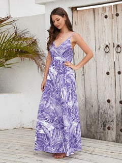 Model wearing a printed surplice spaghetti strap dress with purple leaf patterns, standing against a wooden backdrop.