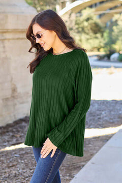 Woman wearing a dark green ribbed long sleeve knit top, paired with sunglasses, walking outdoors.
