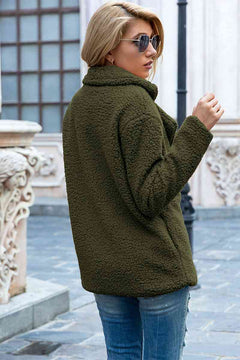 Woman in an olive green lapel collar sherpa coat, stylishly posed outdoors with sunglasses.