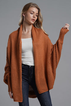 Model wearing a rust-colored dolman sleeve longline cardigan with ribbed details, styled casually with a white top and jeans.