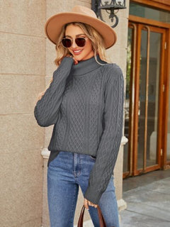 Woman wearing a gray cable-knit mock neck sweater with stylish sunglasses and a hat, posing outdoors.