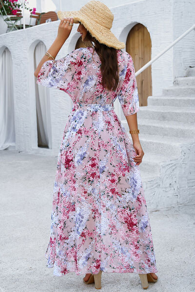 Back view of a woman wearing a pink floral printed tied half sleeve slit dress with a straw hat.