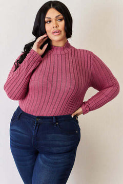Plus size model wearing a pink ribbed mock neck long sleeve t-shirt, paired with blue jeans, showcasing a stylish casual look.
